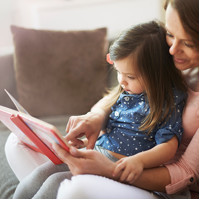 Kleines Mädchen sitzt auf dem Schoss ihrer Mutter und bekommt aus einem Kinderbuch vorgelesen