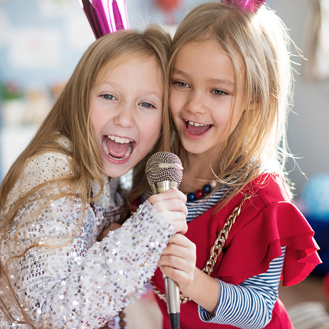 Zwei verkleidete junge Mädchen singen in ein Mikrophon